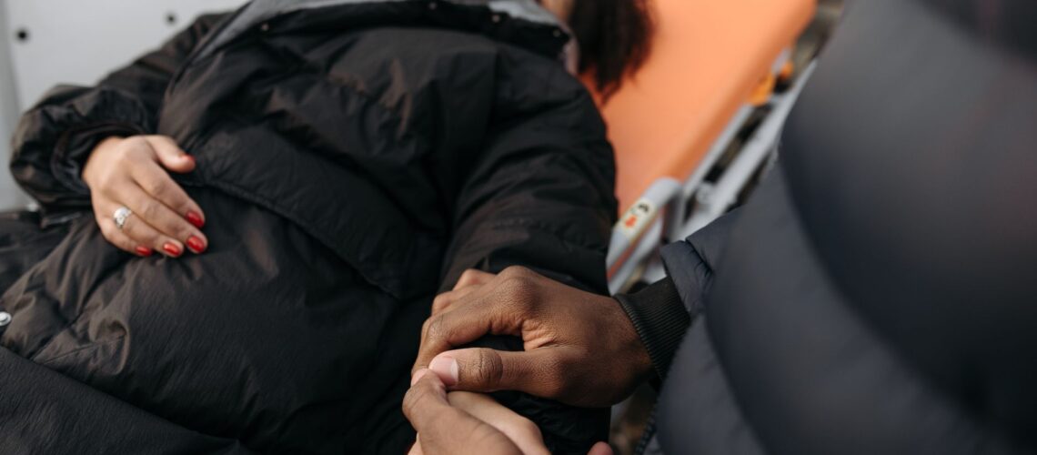 A woman lying on a stretcher as a comforting hand holds hers. Indoor medical care scene.