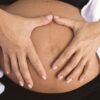 Close-up of a pregnant belly with hands forming a heart shape, symbolizing love and motherhood.