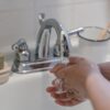 Hands washing under a faucet with running water, emphasizing hygiene and cleanliness.