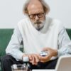 Elderly man with eyeglasses carefully examining his medication while seated on a green couch.