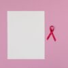 Pink background with a blank paper and a red ribbon symbolizing breast cancer awareness.