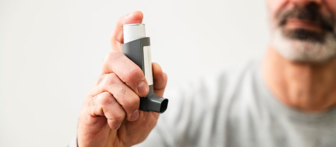 Middle-aged man using an inhaler to manage respiratory issues indoors.