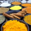 Colorful assortment of spices in bowls with cinnamon sticks on a wooden surface.