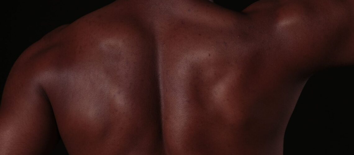 Close-up of a muscular man's back, showcasing defined skin and muscles in a studio setting.
