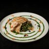 Plate of grilled chicken with greens and vegetables, artfully presented.