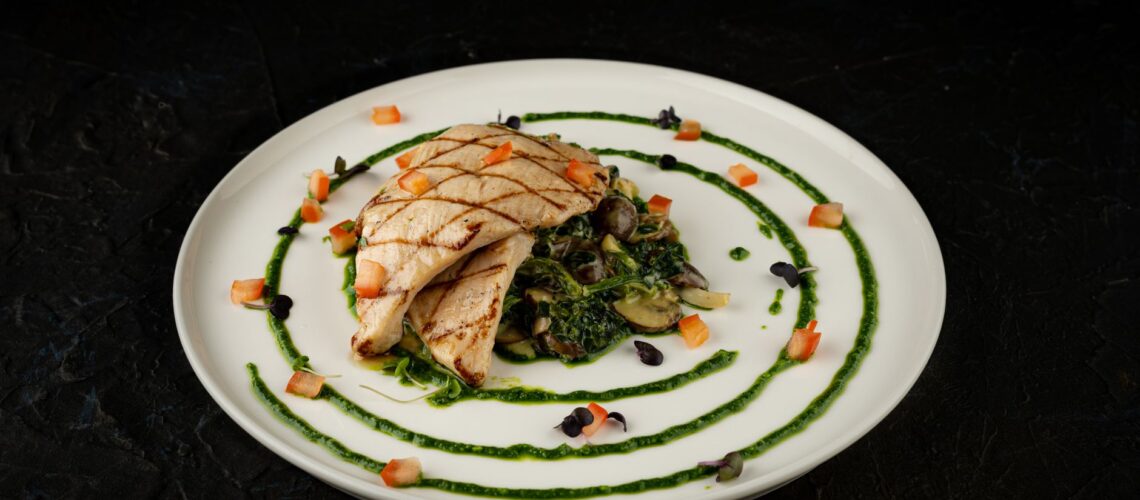Plate of grilled chicken with greens and vegetables, artfully presented.