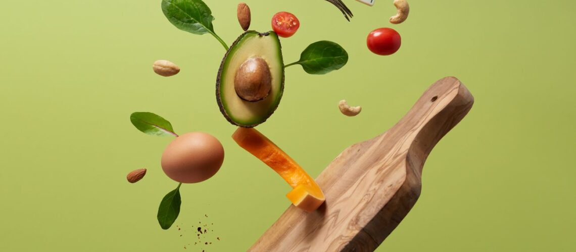 A creative arrangement of paleo diet ingredients floating above a wooden board on a green background.