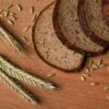 A rustic arrangement of sliced wheat bread with wheat ears and grains on a wooden surface.
