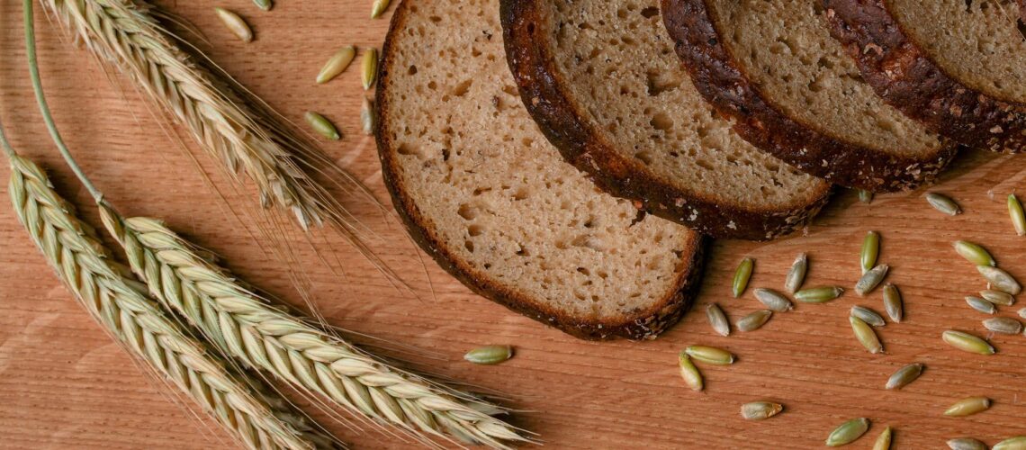 A rustic arrangement of sliced wheat bread with wheat ears and grains on a wooden surface.