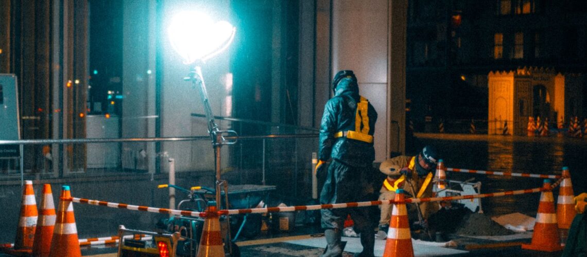 Construction workers at night in a city with bright lights and reflections.