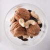 A close-up top view of assorted nuts including walnuts, cashews, and pumpkin seeds in a glass bowl.