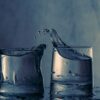 Close-up of splashing water between two glasses on a blue background.