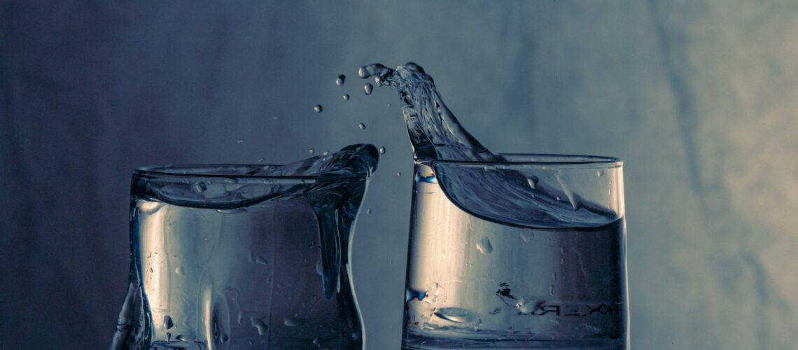 Close-up of splashing water between two glasses on a blue background.