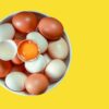 White and brown eggs in a bowl against a vibrant yellow background. Perfect for food photography.