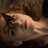 A captivating close-up of a woman with a monarch butterfly on her face, conveying serenity.