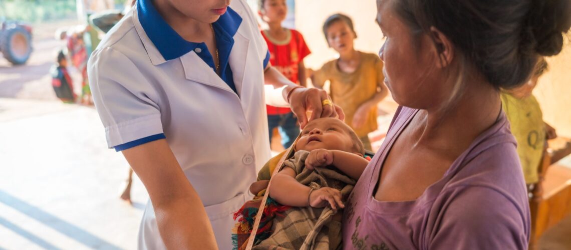 Healthcare worker assisting mother with infant in rural Laos clinic.