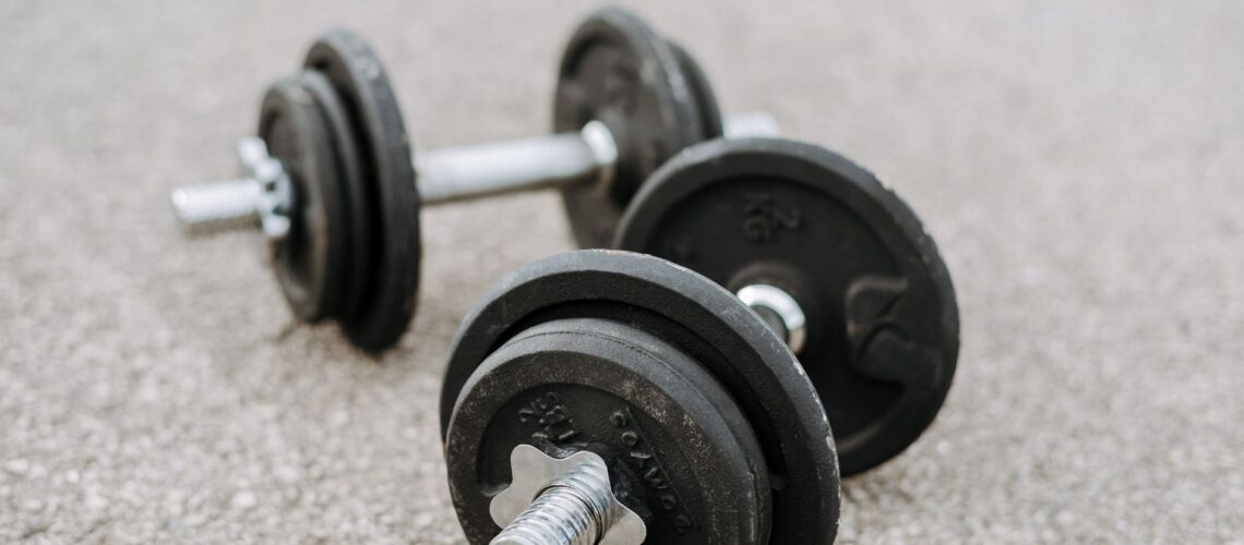 Massive metal dumbbells prepared for difficult healthy training on asphalt road in summer