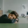 A contemplative child rests on a desk in a quiet classroom setting.