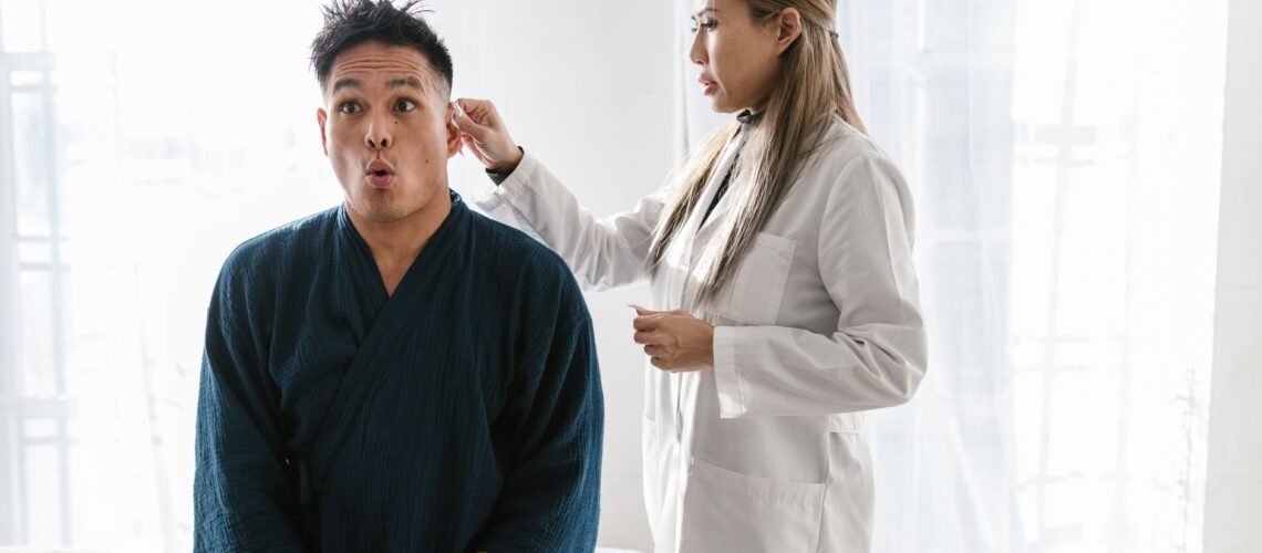 A doctor in a white coat conducts an ear exam on a patient indoors.