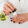 Close-up of a woman's hands applying serum to nails with a dropper in a bathrobe.