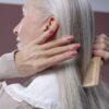 Elderly woman with silver hair combing her hair, highlighting graceful aging and care.