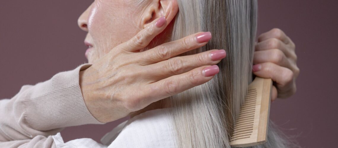 Elderly woman with silver hair combing her hair, highlighting graceful aging and care.
