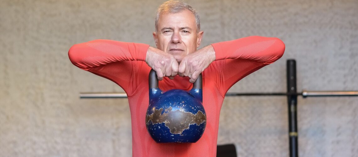 Elderly man engages in strength training with kettlebell, promoting fitness and healthy aging.