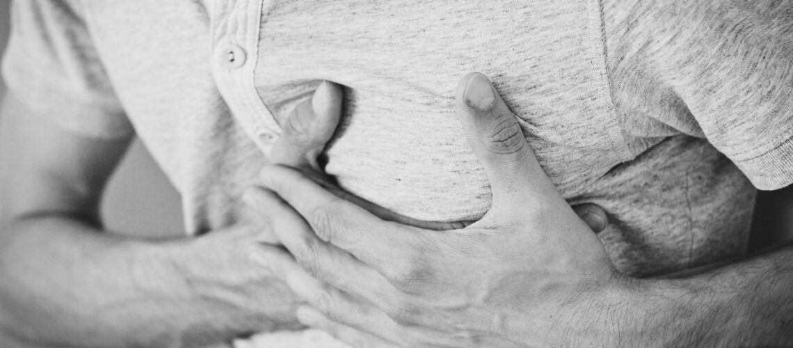 Black and white photo of a man clutching his chest, indicating discomfort or pain.