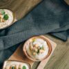 Top view of creamy homemade hummus in bowls with chickpeas and herbs on a wooden table.