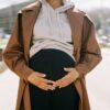 A stylish pregnant woman with hands on her belly in a modern urban environment.