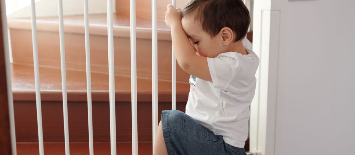 A curious toddler climbing a safety gate near stairs inside a home.