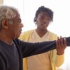A caregiver helps an elderly man with arm exercises in a warm and caring environment.