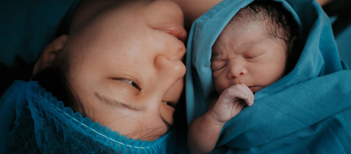 A touching image of a mother and her newborn baby wrapped in blue medical blankets.