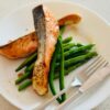 Delicious grilled salmon fillet served with fresh green beans on a white plate, perfect for a healthy meal.