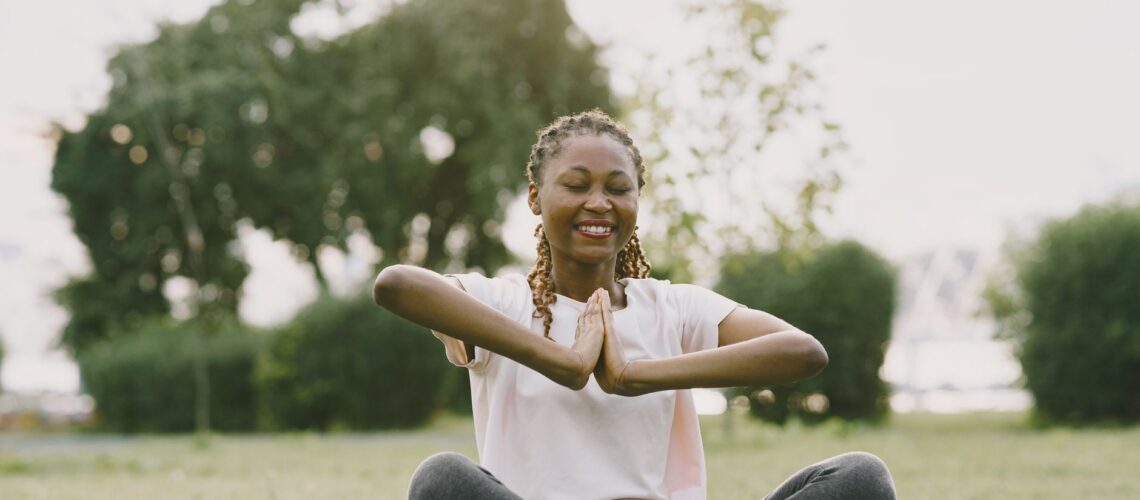 African American woman practicing yoga in a sunny park, enjoying relaxation and wellness outdoors.