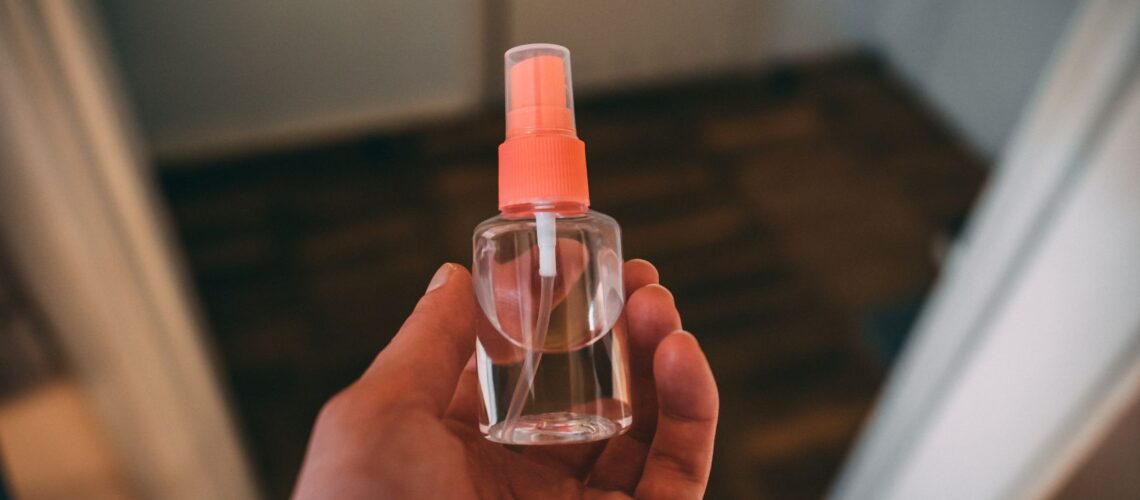 Close-up of a hand holding a clear plastic spray bottle indoors, suitable for healthcare use.