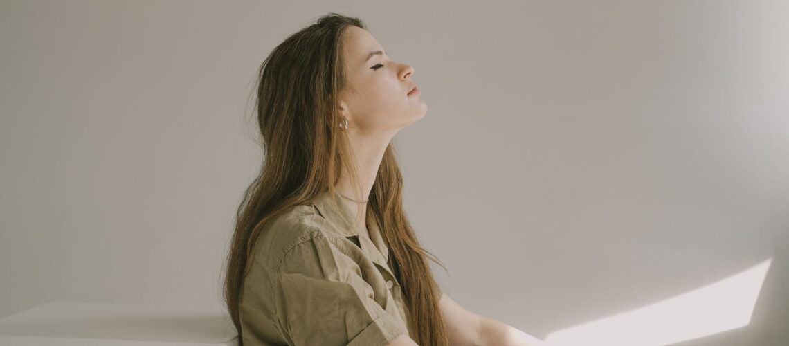 Side profile of a young woman sitting indoors, lost in thought with eyes closed.