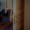 Elderly man sits pensively in an armchair in a warmly decorated room, conveying solitude.