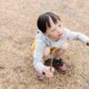 Young boy with Down syndrome enjoying outdoor play, crouching and holding a stick.