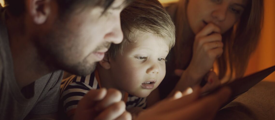 A family of three, including parents and a child, intently watching a digital tablet together indoors.