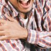 Close-up of a man in plaid shirt experiencing shoulder pain, grasping his arm.