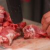 Close-up view of hands cutting raw meat with a knife on a chopping board, ideal for culinary or food safety topics.