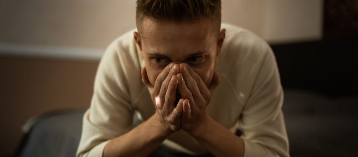 A worried man indoors covering his face with hands, depicting stress or contemplation.