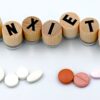 Wooden blocks spelling 'Anxiety' with assorted pills below on a light background.