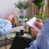 Unrecognizable professional therapist writing on clipboard while sitting against male client lying on couch on blurred background during mental health therapy
