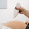 Close-up of a pregnant woman's belly with ultrasound gel being applied for a sonography session.