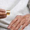 Close-up of elderly hands applying serum with dropper, focusing on skincare and aging.