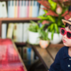 Adorable child in a straw hat and sunglasses sitting in a library with plants.