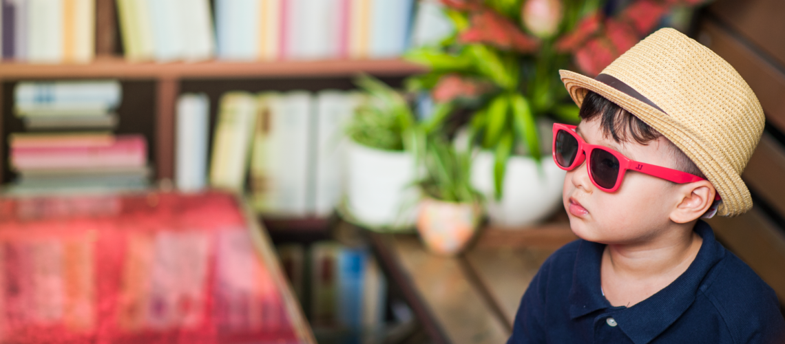 Adorable child in a straw hat and sunglasses sitting in a library with plants.