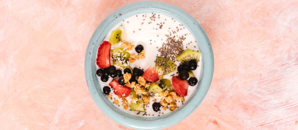 Top view of a nutritious breakfast bowl with yogurt, fresh fruits, and seeds on a pink background.